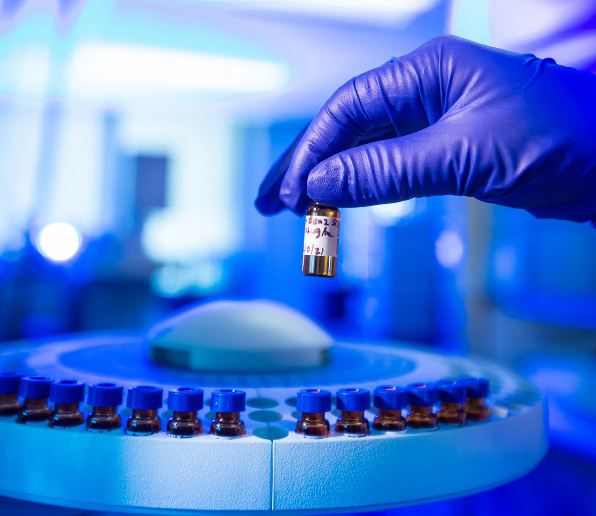 Gloved hand holding a reconstituted research vial above an autosampler tray